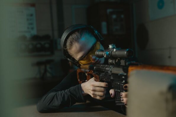 Woman aiming precision rifle with scope at indoor range