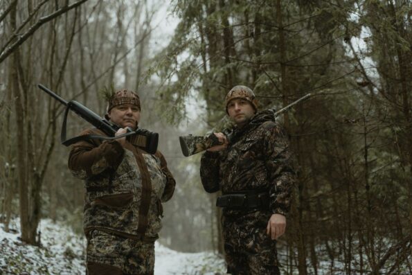 Two hunters in camouflage with rifles in snowy forest - deer hunting